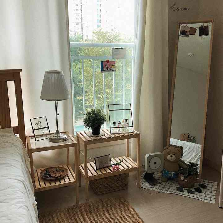 ナチュラルな木目調と白を基調とした寝室、ナイトテーブルとフロアランプ、床置きの鏡が印象的に配置された空間