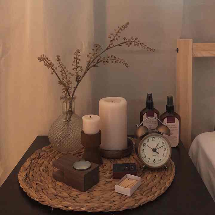 Cozy bedroom nightstand in warm wood and beige tones featuring aroma spray, candles, and a vintage alarm clock