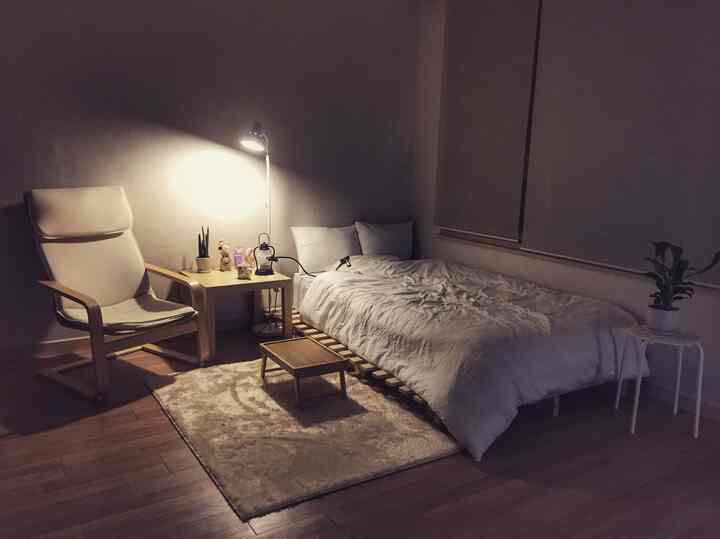 Small bedroom in white and wood tones featuring a bed frame, armchair, and floor lamp creating a cozy atmosphere