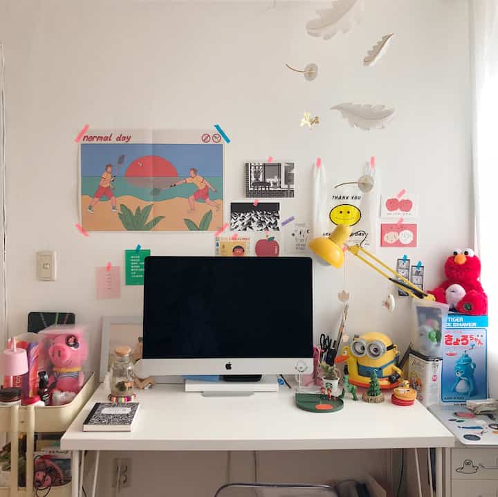 白色の壁とデスクが配置されたホームオフィス空間、壁にはかわいい小物やポスターが飾られた温かみのあるインテリア
