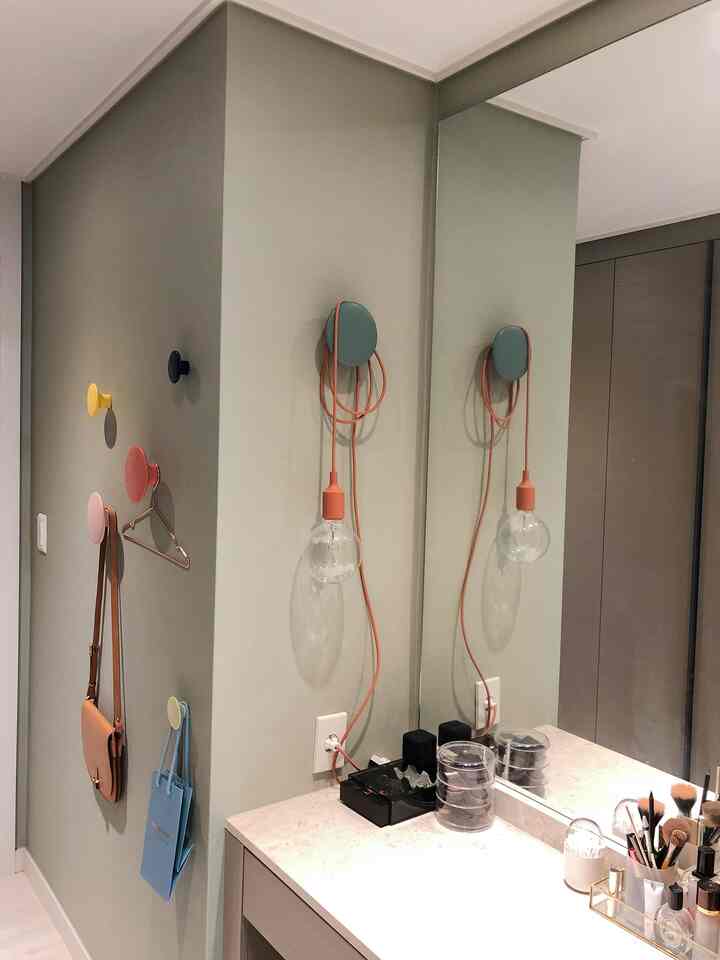 Powder room with soft green walls, colorful coat hooks, and an orange pendant light, featuring a modern vanity and built-in closet