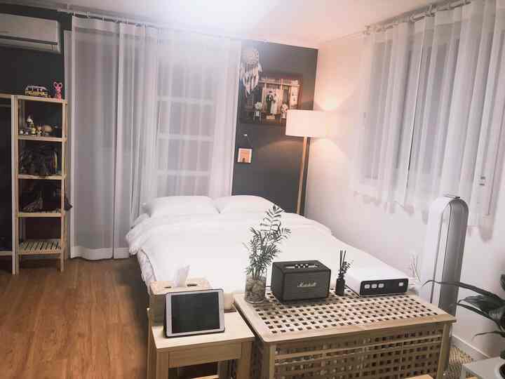 ホワイトと木目調が調和する寝室、中央に配置されたダブルベッドとナイトテーブル、木製の棚が雰囲気ある空間を演出