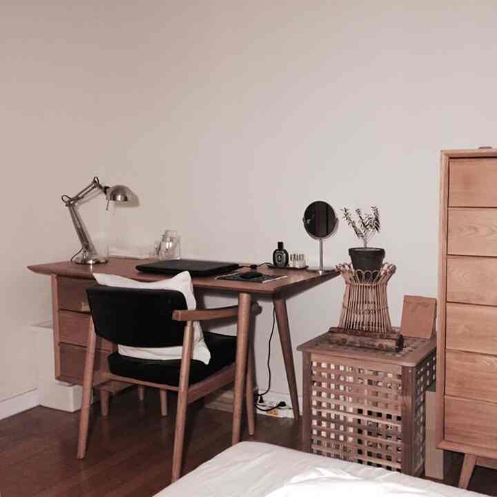 Natural wood-toned and simple studio bedroom workspace featuring wooden desk and chair, white walls, and a potted plant