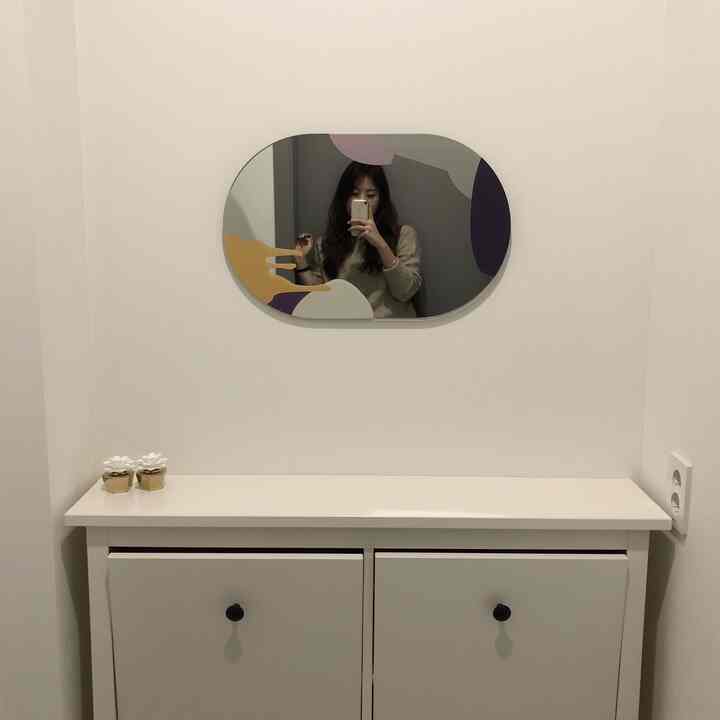 White-walled narrow entrance space featuring a white shoe cabinet topped with a uniquely patterned mirror, creating a cozy atmosphere