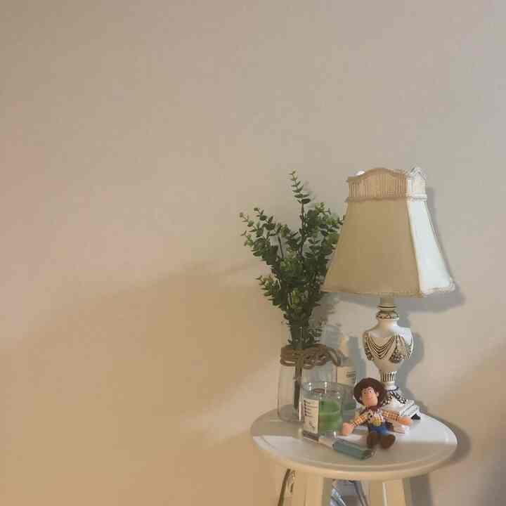 White and wood tone bedroom corner with side table featuring lamp, artificial plant, and candle in a minimalist style
