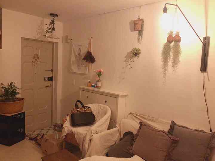 暖かい照明とホワイトトーンの2人用リビング、ラタンのアームチェアと植物が配置された自然で居心地の良いインテリア