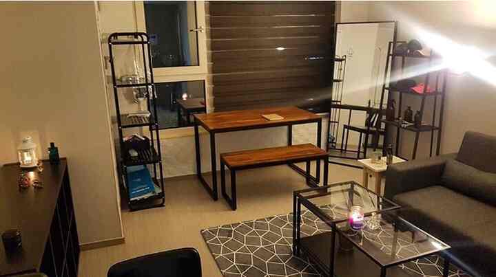 Modern living room with natural wood tone dining set and black metal frames, featuring a geometric rug and simple furniture layout