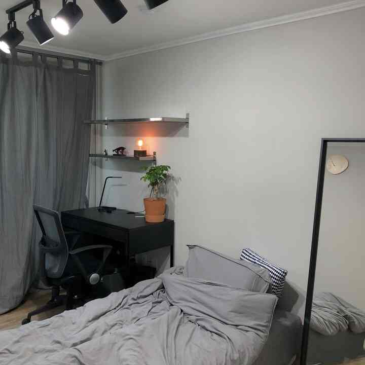 Gray and white toned bedroom featuring a black desk and office chair, wall shelves, and curtains, creating a modern minimal space