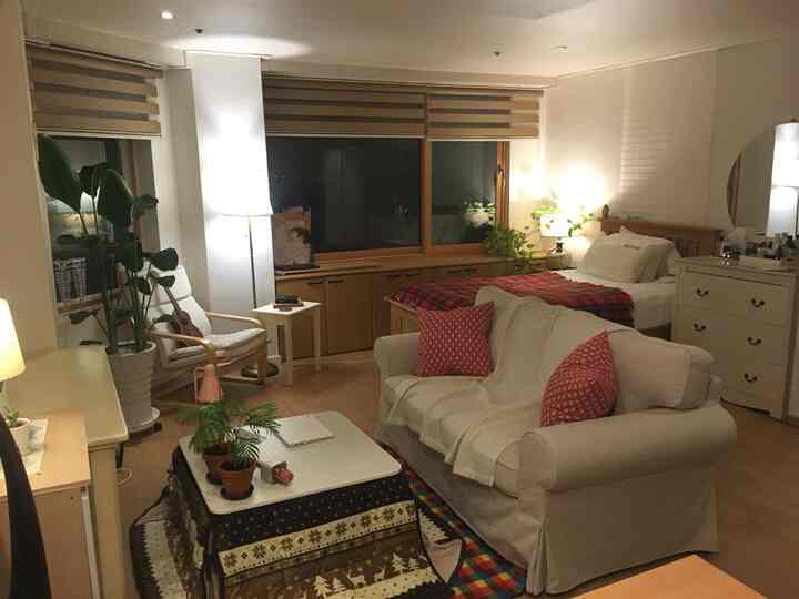 Natural tone studio apartment bedroom-living room with white and red accents, featuring sofa and armchair for cozy atmosphere