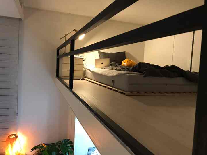 Natural color loft bedroom featuring a low wood pallet platform bed, nightstand, and task lamp in a cozy setting