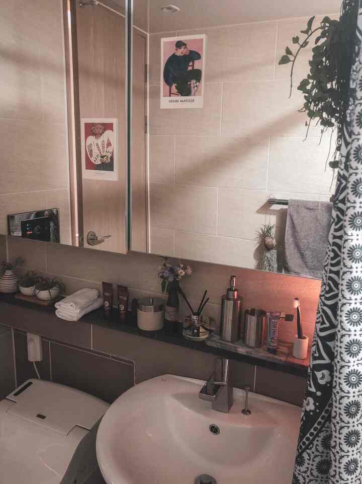 ベージュ色の壁と白い洗面台があるバスルーム、棚にはディフューザーやタオルが置かれ、自然で落ち着いた雰囲気のインテリア