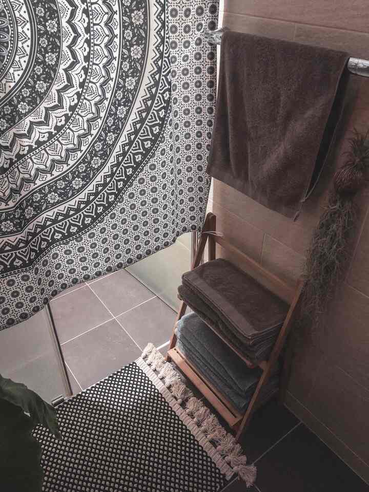 Bathroom with natural tones and patterned curtain, featuring towels and wooden shelf creating a resort-like ambiance