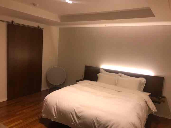 Simple bedroom with warm brown wooden floor contrasting white bedding creating a cozy atmosphere