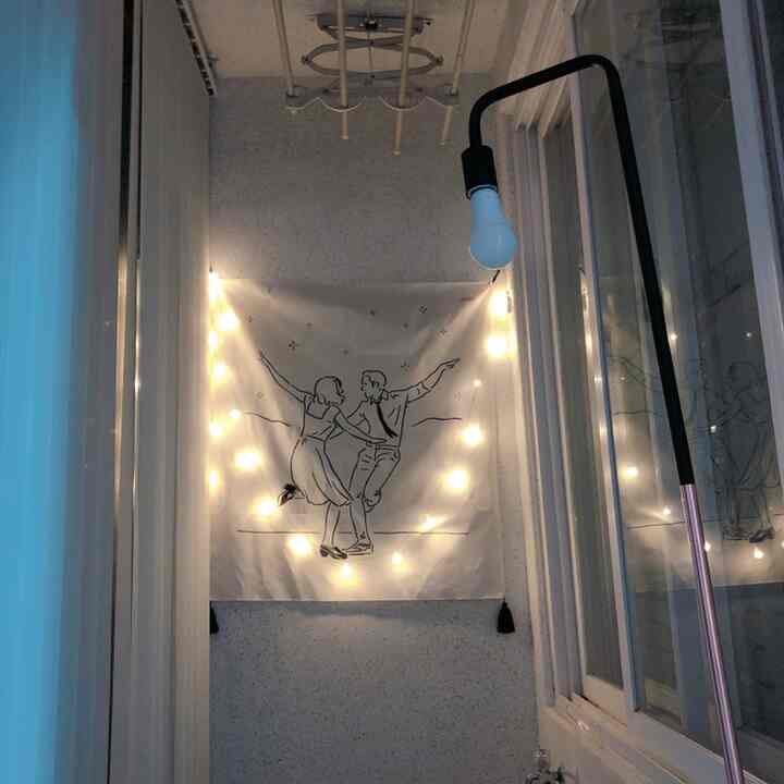 White-toned narrow room featuring a fabric poster with couple illustration and string lights, creating a cozy seated space