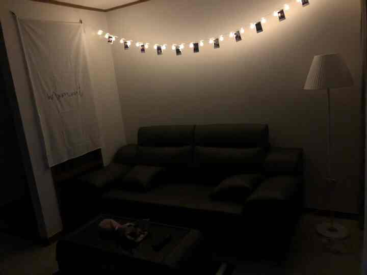 薄暗い照明の中に黒いソファと白いフロアランプが置かれたミニマルなリビングルーム