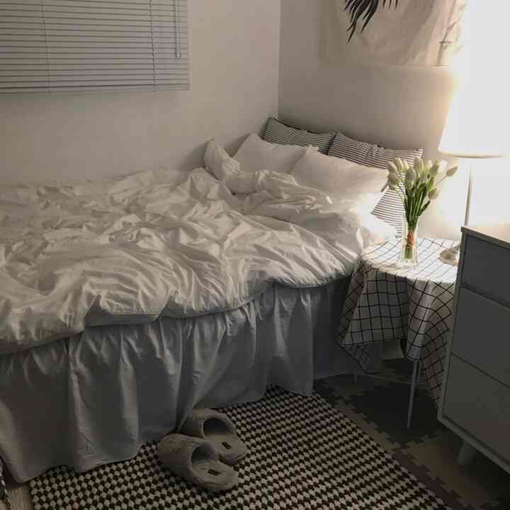 白を基調とした寝室、居心地の良いベッドと整ったナイトテーブル、花束が置かれた雰囲気のあるインテリア