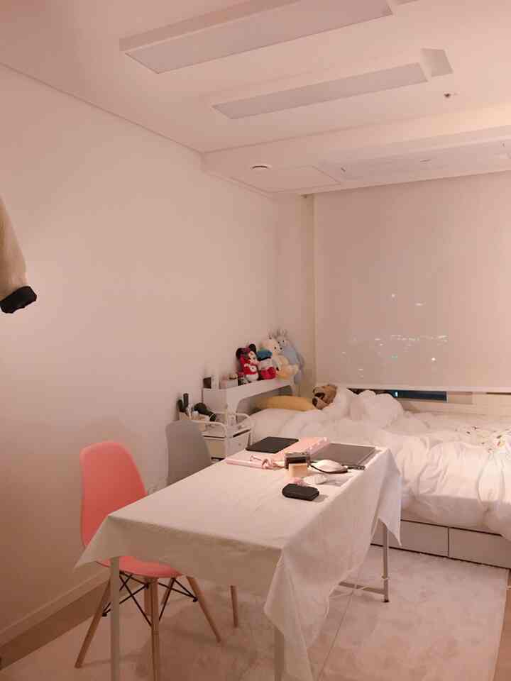 白を基調としたコンパクトな寝室、収納ベッドと白いテーブルクロスをかけたテーブルが配置された落ち着いた空間