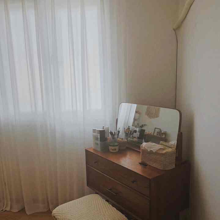 Natural tone small room featuring white chiffon curtains and a wooden vanity with a mirror