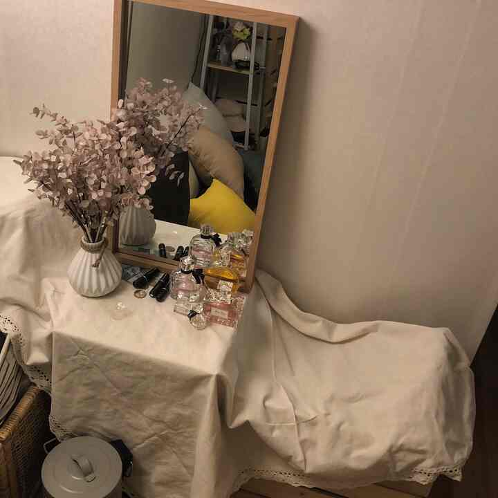 Natural tone vanity area with beige fabric-covered table and stool, wooden framed mirror, and artificial eucalyptus plant