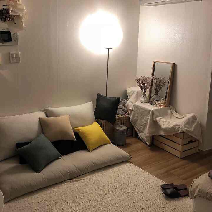 Beige and natural tone studio living room featuring floor lamp and cushioned floor sofa creating a warm atmosphere
