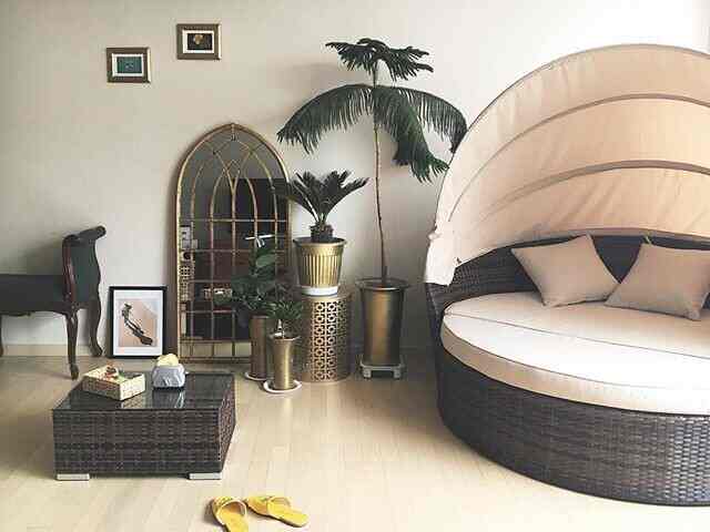 ゴールドのトーンが印象的なアジアンスタイルのリビング、ラタンのサンベッドとコーヒーテーブル、観葉植物が配置された雰囲気のあるインテリア