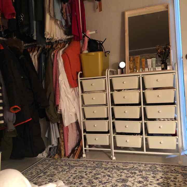A white-toned walk-in closet featuring an L-shaped clothes rack and multiple drawer units with a cozy, organized atmosphere