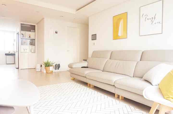 Bright white and beige toned living room featuring a beige sofa and yellow wall art, simple and natural atmosphere