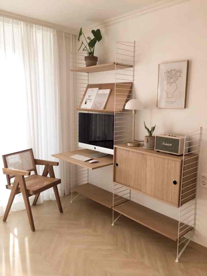 Bright natural wood-toned living room home office featuring string system and rattan armchair in a minimalist modern style