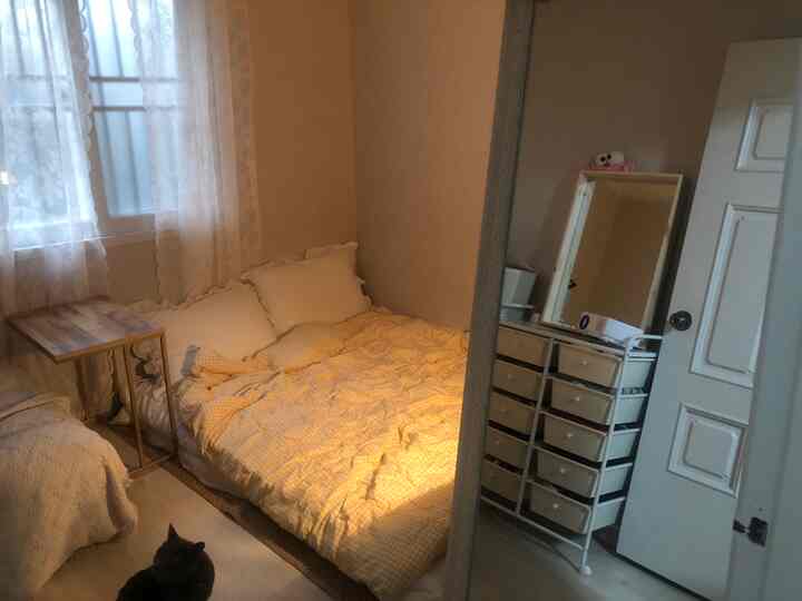 A compact bedroom with white walls and yellow checkered mattress, featuring a storage chest and large full-length mirror creating a cozy atmosphere