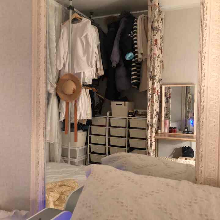 ベージュの色調のワンルーム、 大型鏡と白い寝具、クローゼットと収納が配置された落ち着いたコンパクトなインテリア