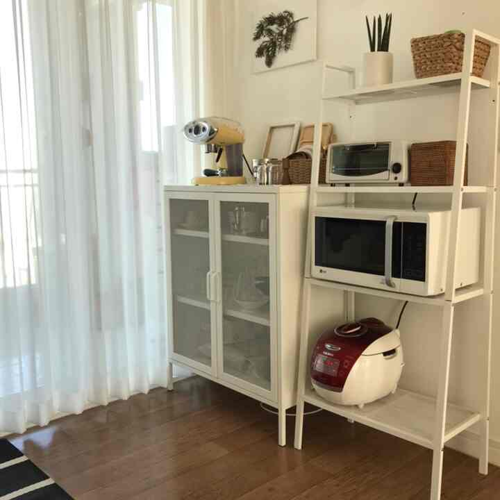 Bright and tidy white-toned kitchen featuring shelves with a microwave, rice cooker, and coffee machine in a modern setup