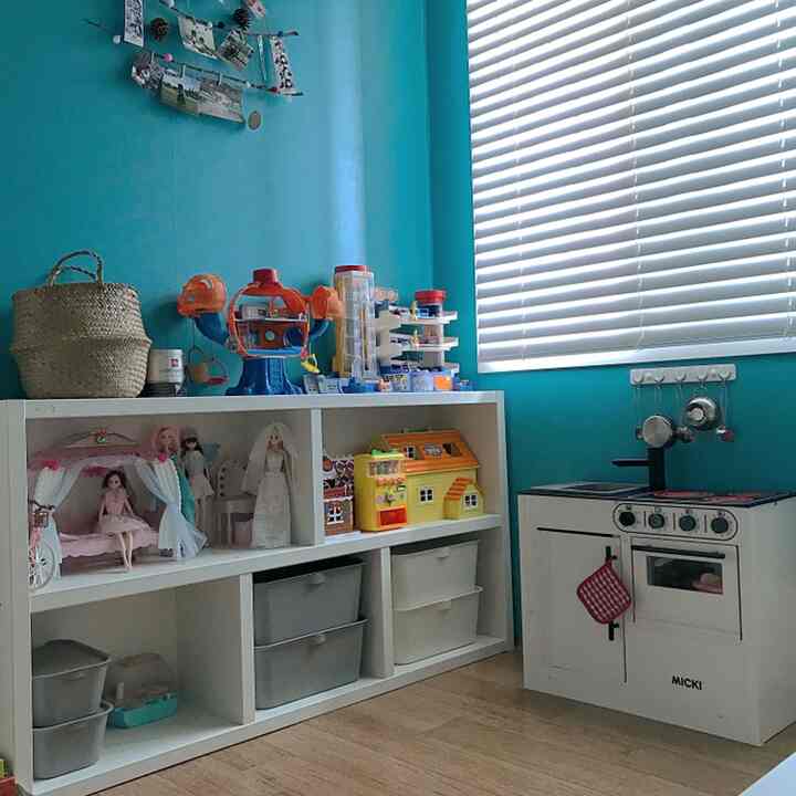 青い壁と白い収納棚がある子供部屋、おもちゃと遊び用キッチンが配置された雰囲気のある空間