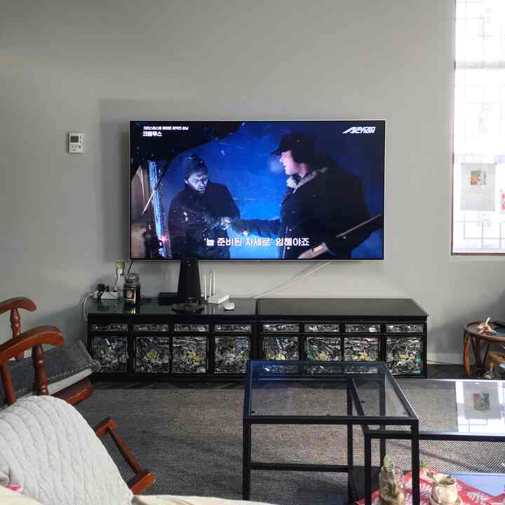 Bright gray-walled living room with white sofa, mother-of-pearl cabinet centered under wall-mounted TV, complemented by black metal coffee table