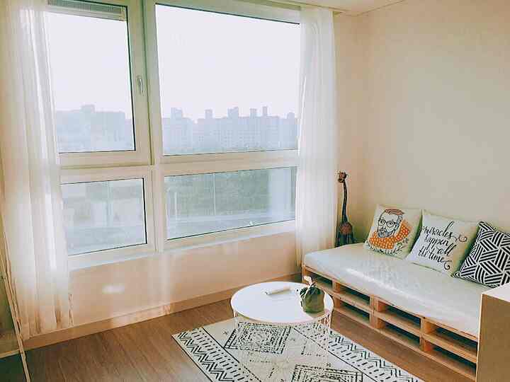 Bright white and brown toned small living room with sheer curtains by large windows, pallet sofa, and round coffee table in a natural Nordic style