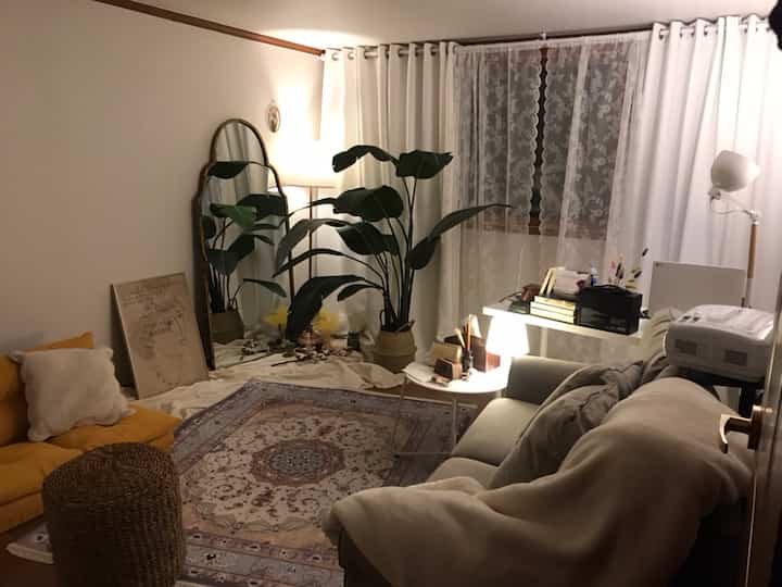 Beige and white toned living room featuring sofa, large mirror, plants, and lighting creating a cozy atmosphere