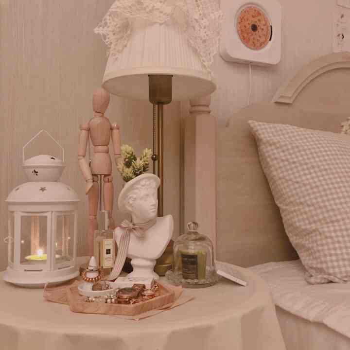 Warm beige bedroom nightstand featuring plaster bust plant pot, candle holder, and wooden mannequin creating a cozy ambiance