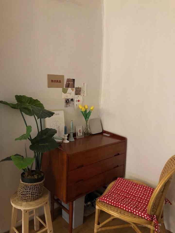 ベージュ色の壁と木製家具、植物とクッションが配されたナチュラルスタイルの小さな部屋の化粧台スペース