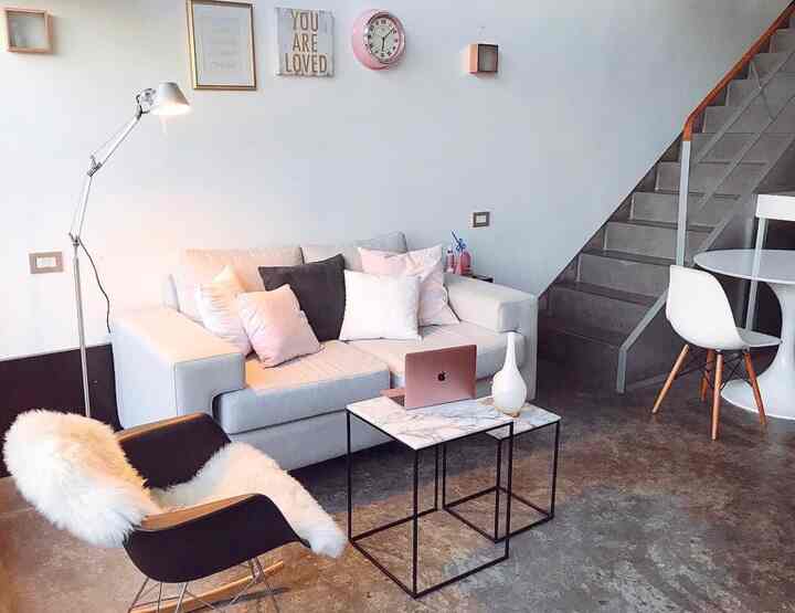 A modern and cozy living room in white and pink tones featuring a sofa, marble coffee tables, and loft stairs