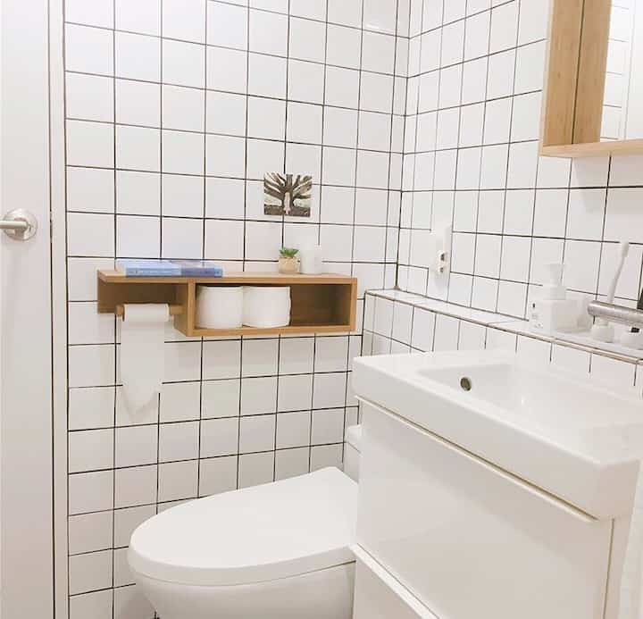 White and wood-toned bathroom featuring custom wooden toilet paper holder and clean sink, creating a cozy and neat atmosphere