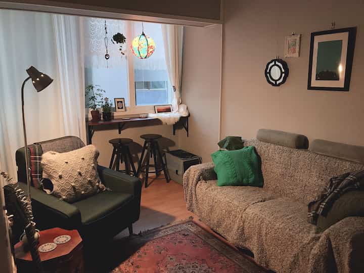 Beige and green tone studio living room featuring sofa, armchair, and small bar stools with a cozy atmosphere
