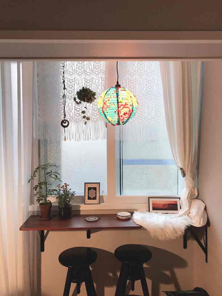 白いカーテンとレースが調和する窓辺、木製カウンターテーブルとスツールが配置されたカフェ風の落ち着いた空間