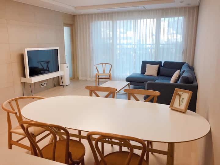 White and wood tone living room featuring a wood dining table, sofa, and sheer curtains in a modern and simple space
