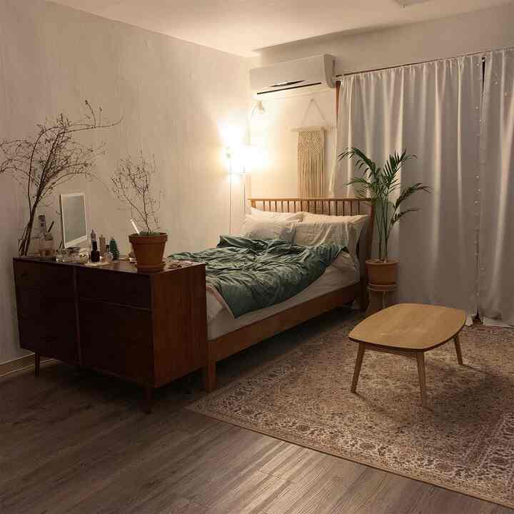 Natural-toned bedroom featuring wooden bed and dresser, plants, and curtains creating a cozy atmosphere
