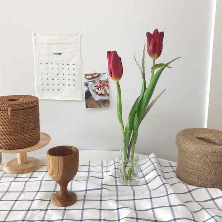 Natural kitchen space with white walls and checkered tablecloth featuring rattan baskets, wooden cup, and red tulips in a clear vase