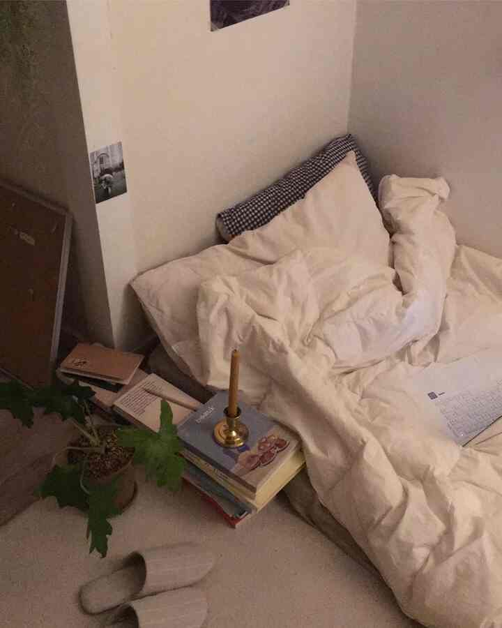 Beige and white toned bedroom featuring a low bed, vintage candle holder, and books creating a cozy atmosphere