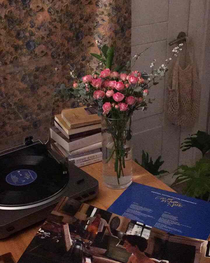 Cozy single household desk space with warm lighting and retro vibes, featuring a vase of flowers and a turntable