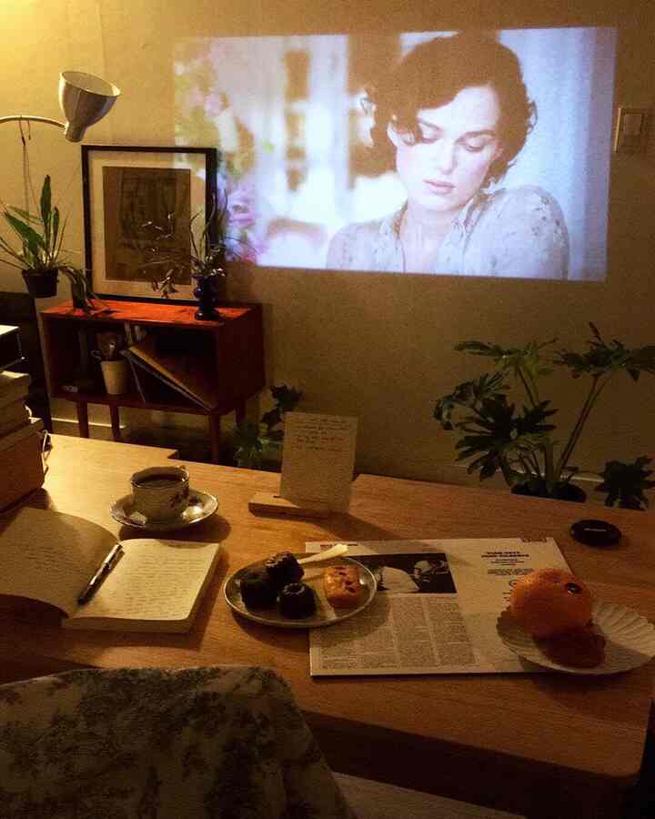 Cozy living room with warm wood tones, coffee cup and desserts on table, enjoying movies projected by mini beam projector in a home cinema setting