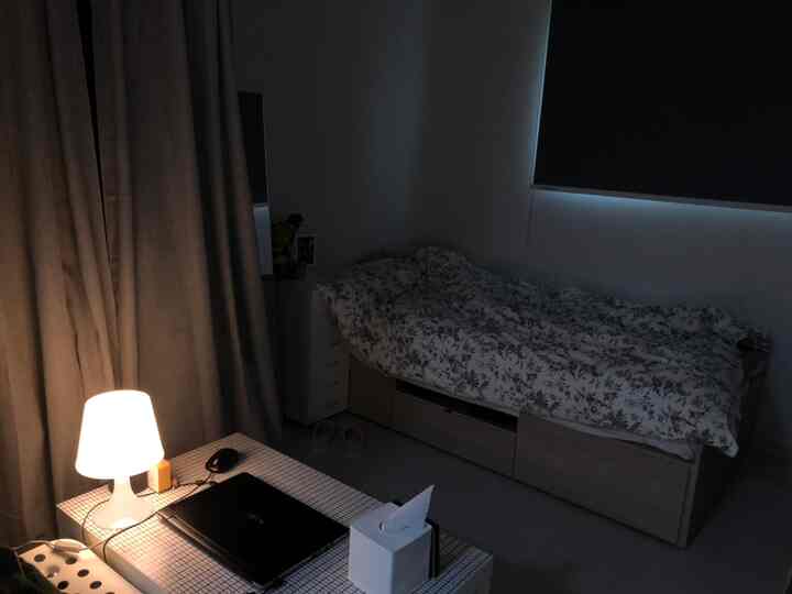 A cozy studio bedroom in white and beige tones featuring a storage bed and table lamp