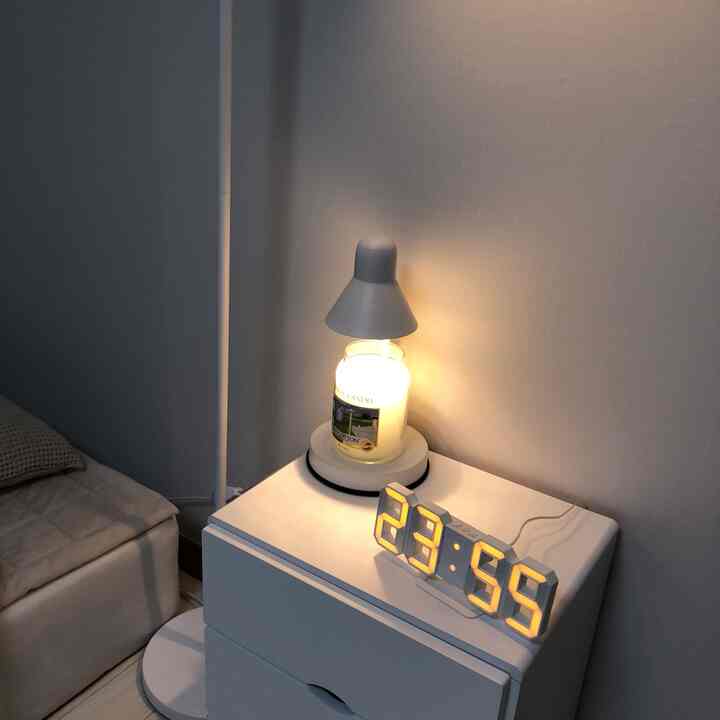白色調のワンルームのナイトテーブルに置かれたミニキャンドルとデジタルLED時計が配置された雰囲気のあるインテリア