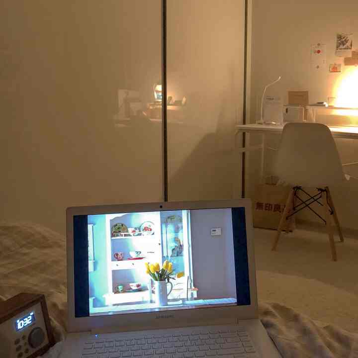 暖かいベージュとアイボリーのトーンのワンルーム寝室、デスクとノートパソコン、照明が配置された居心地の良いシンプルな空間